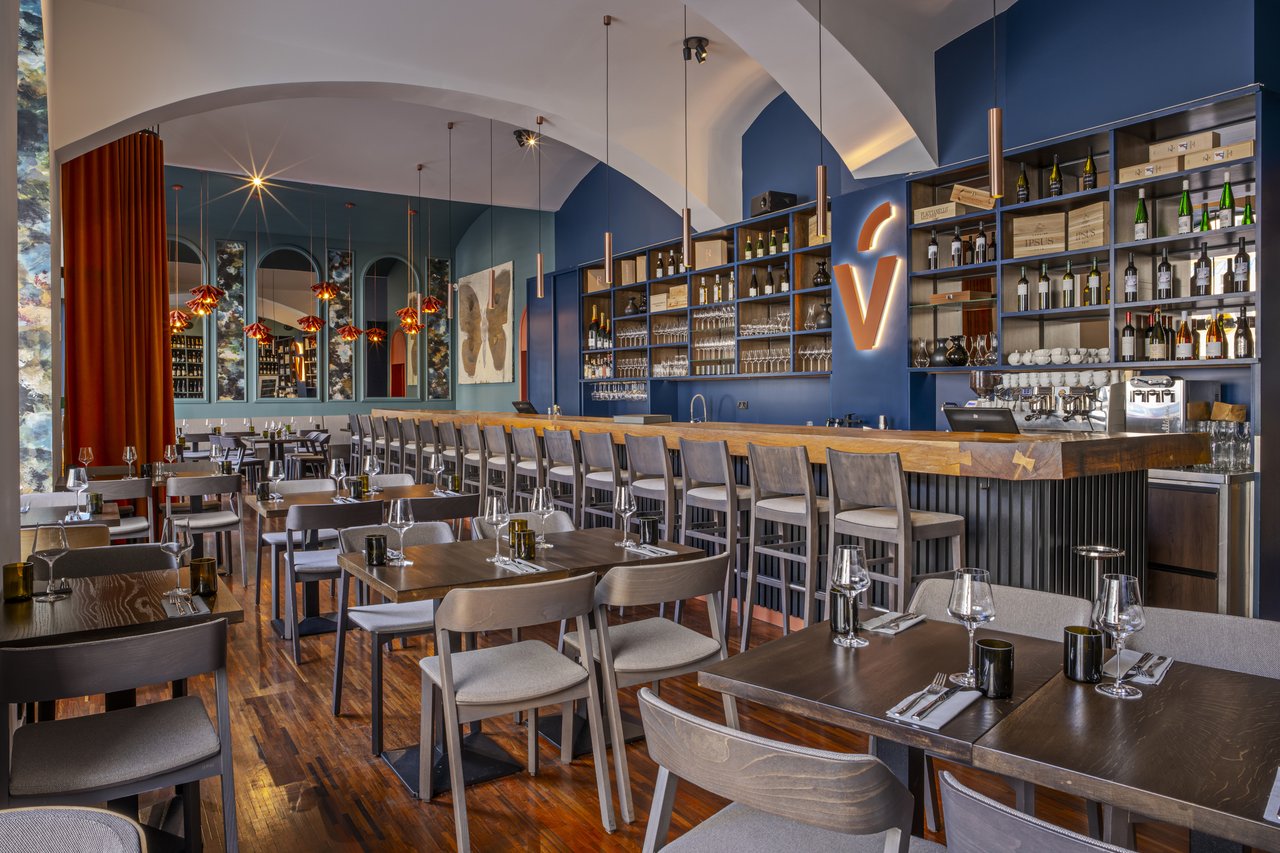 Grande salle de restaurant avec des tables et un bar en fond avec plusieurs bouteilles