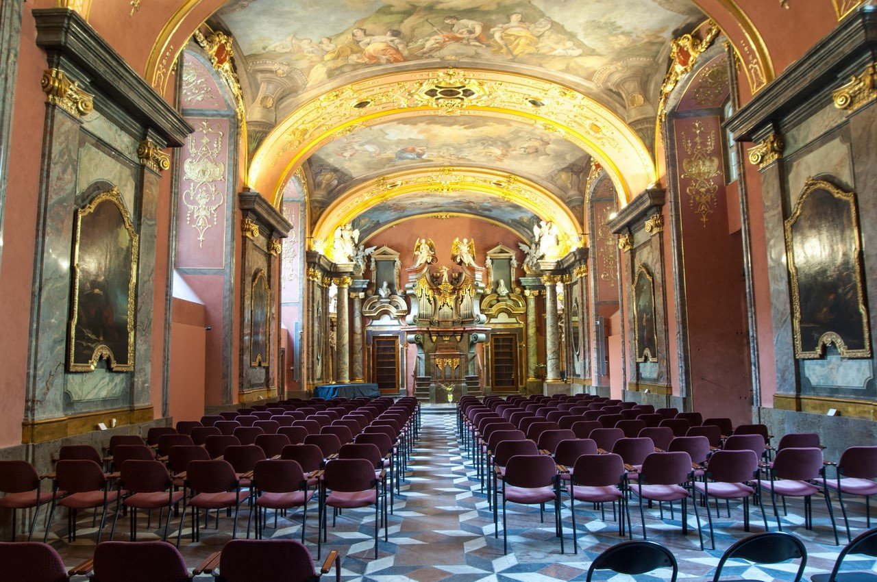 Grand rangé de chaise dans une chapelle avec des murs colorés et ornés d'or avec une peinture sur le plafond