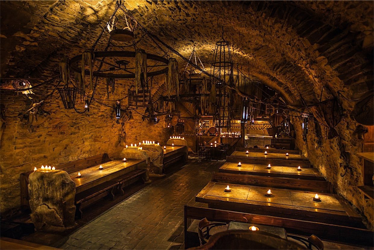 Intérieur du restaurant médiéval les tables sont parsemées de bougies et il y a un grand lustre accroché au plafond