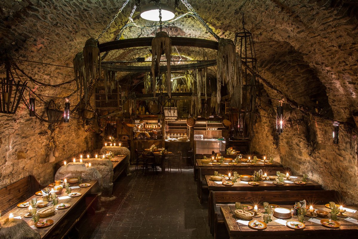 Intérieur restaurant médiéval avec un grand lustre au milieu les tables sont éclairer à la bougie
