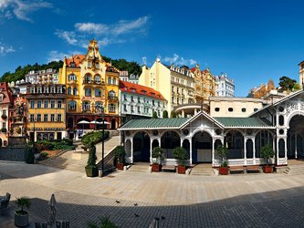 en:A square surrounded by tall, colorful buildings with a long white wooden gallery  carved with lace-like patterns ;fr:Une place entourée de grands bâtiments colorés avec une longue galerie en bois blanc sculptée de dentelles