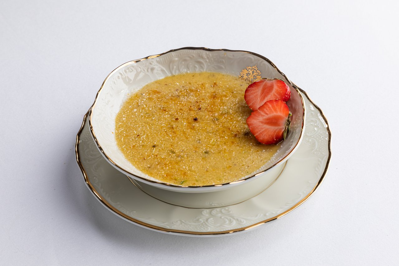 Crème brûlée surplombé de deux fraises dans une vaisselle blanche ornée d'or et de motifs