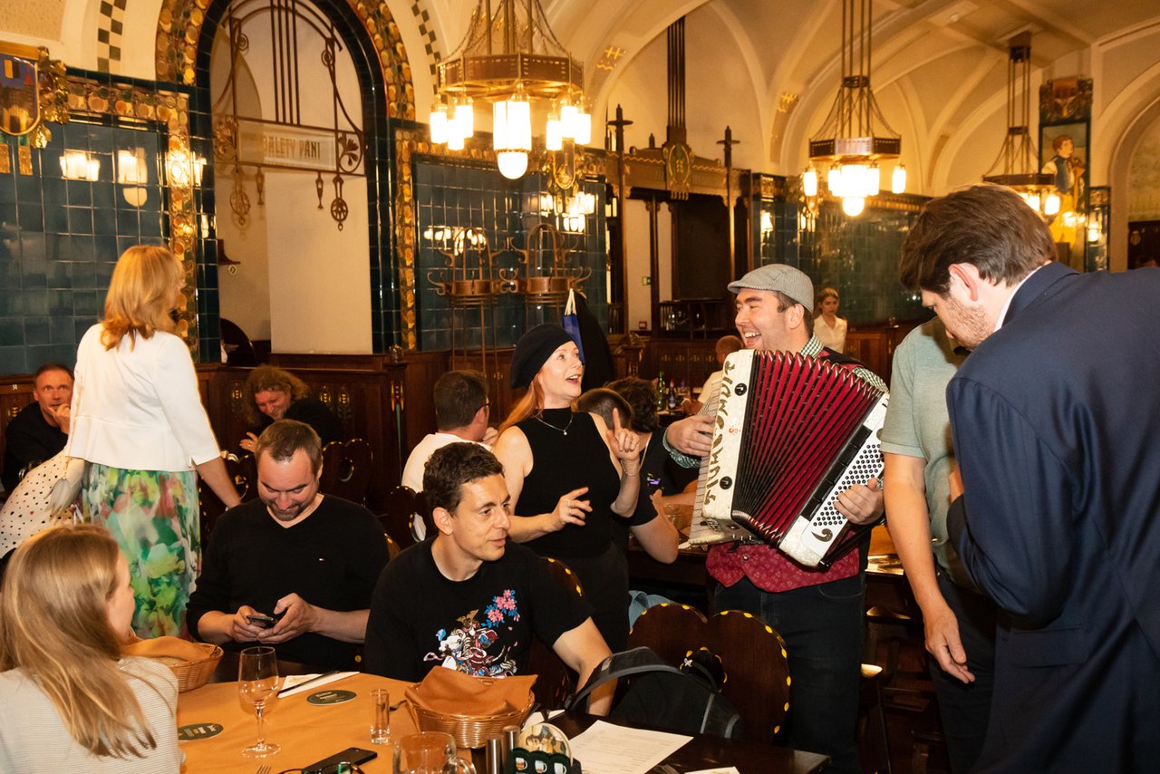 Grandes salles avec beaucoup de personnes et de tables réunies il y a un musicien qui chante de l'accordéon