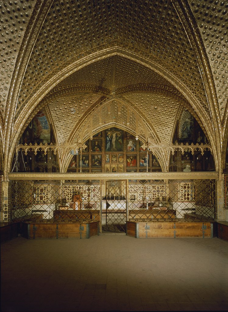 Une arche gothique entièrement recouverte d'or et de décorations, protégée par une grille, avec des peintures en arrière-plan