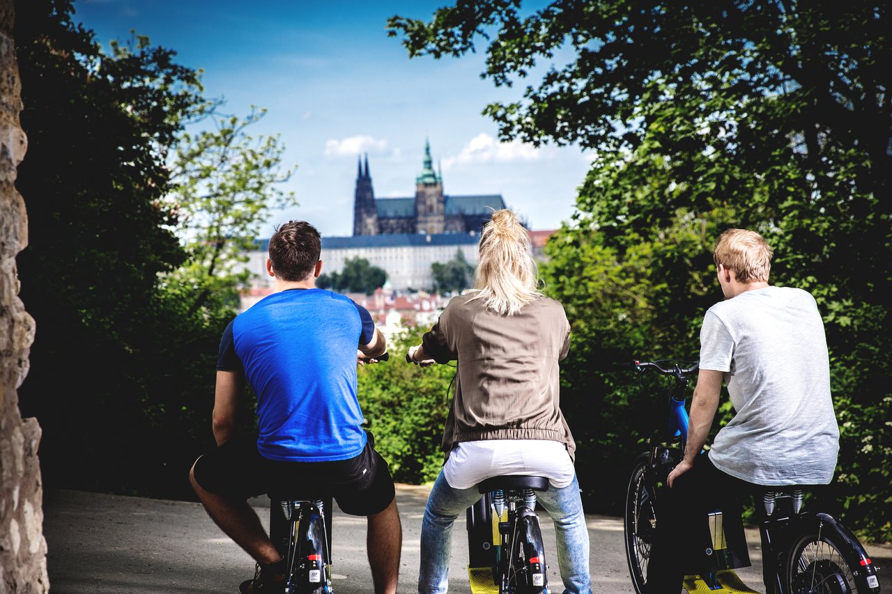 Trois personnes vues de dos sur une trottinette électrique, admirant la vue sur le château