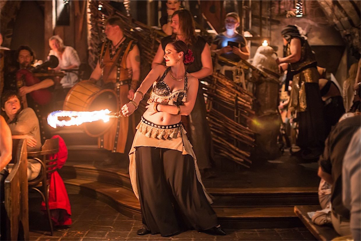 Femme en tenue médiévale qui danse avec un grand bateau enflammé, le public est surpris