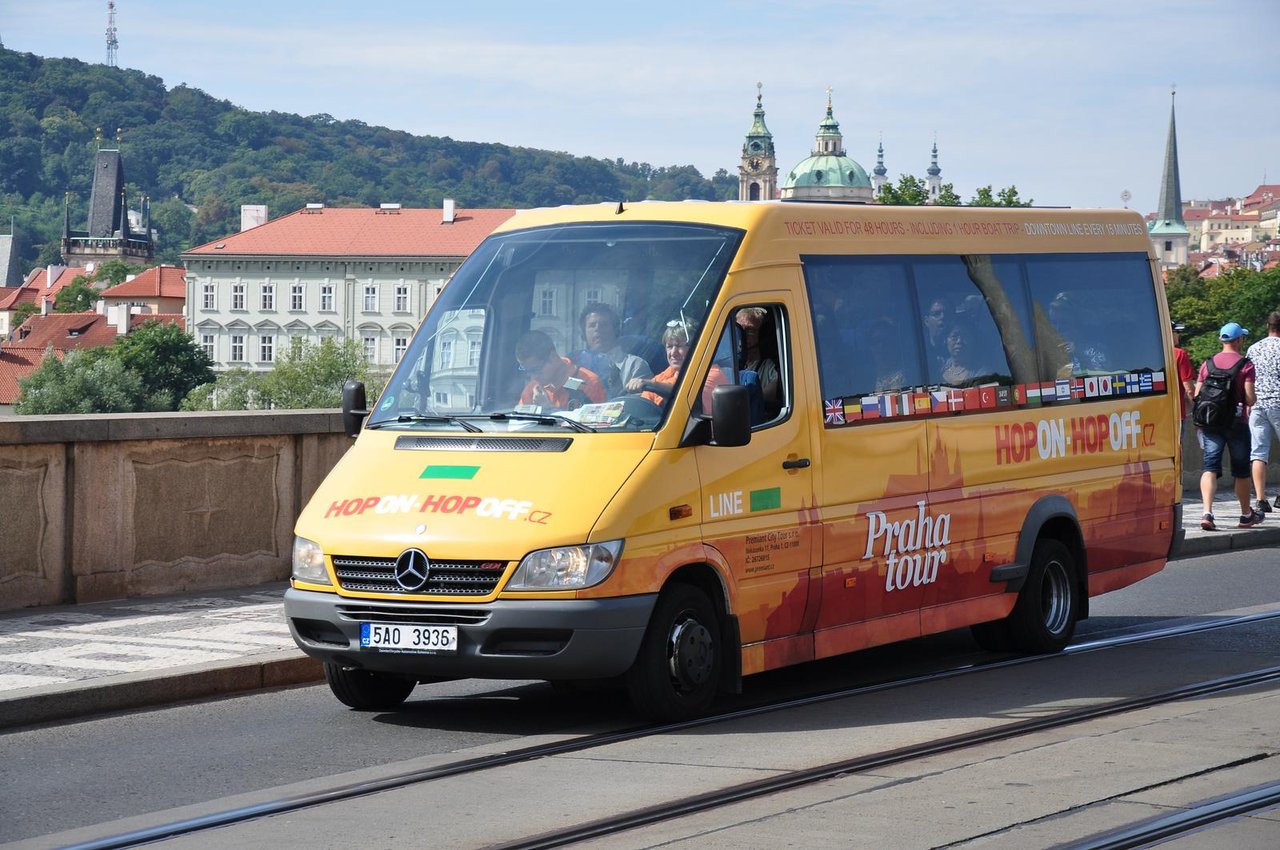 Un minibus touristique orange passe, transportant des touristes à son bord.