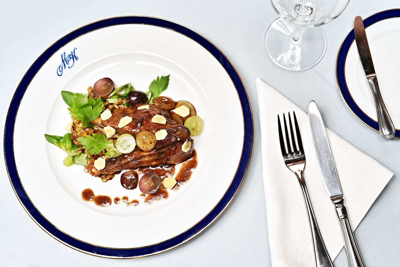 Plats de viande dans une assiette bleu et blanc avec des couvert gris argent et un verre