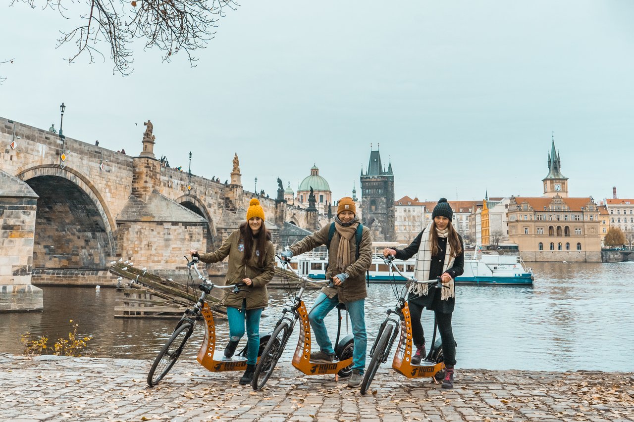 3 personnes sur des trottinettes électriques à l'automne,avec la rivière qui coule sous un vieux pont emblématique en arrière-plan
