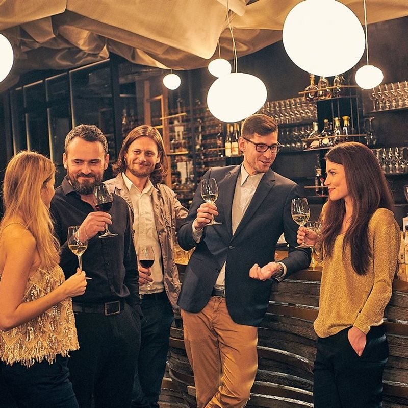 Deux femmes et trois hommes qui boivent un verre de vin et du champagne devant un bar
