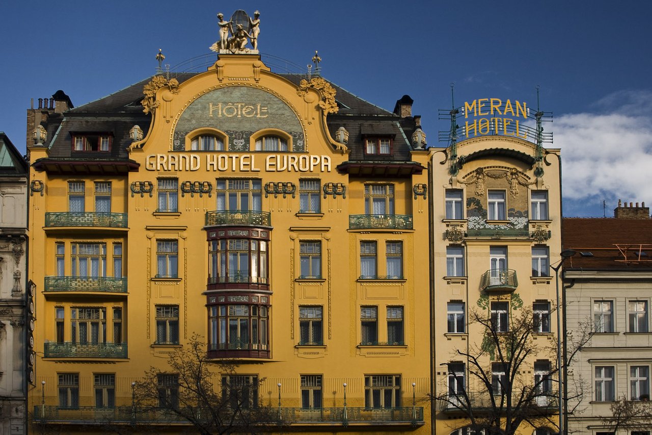 Une grande façade jaune ornée de moulures, avec des balcons verts et l'inscription « Grand Hôtel Europa » sur la façade