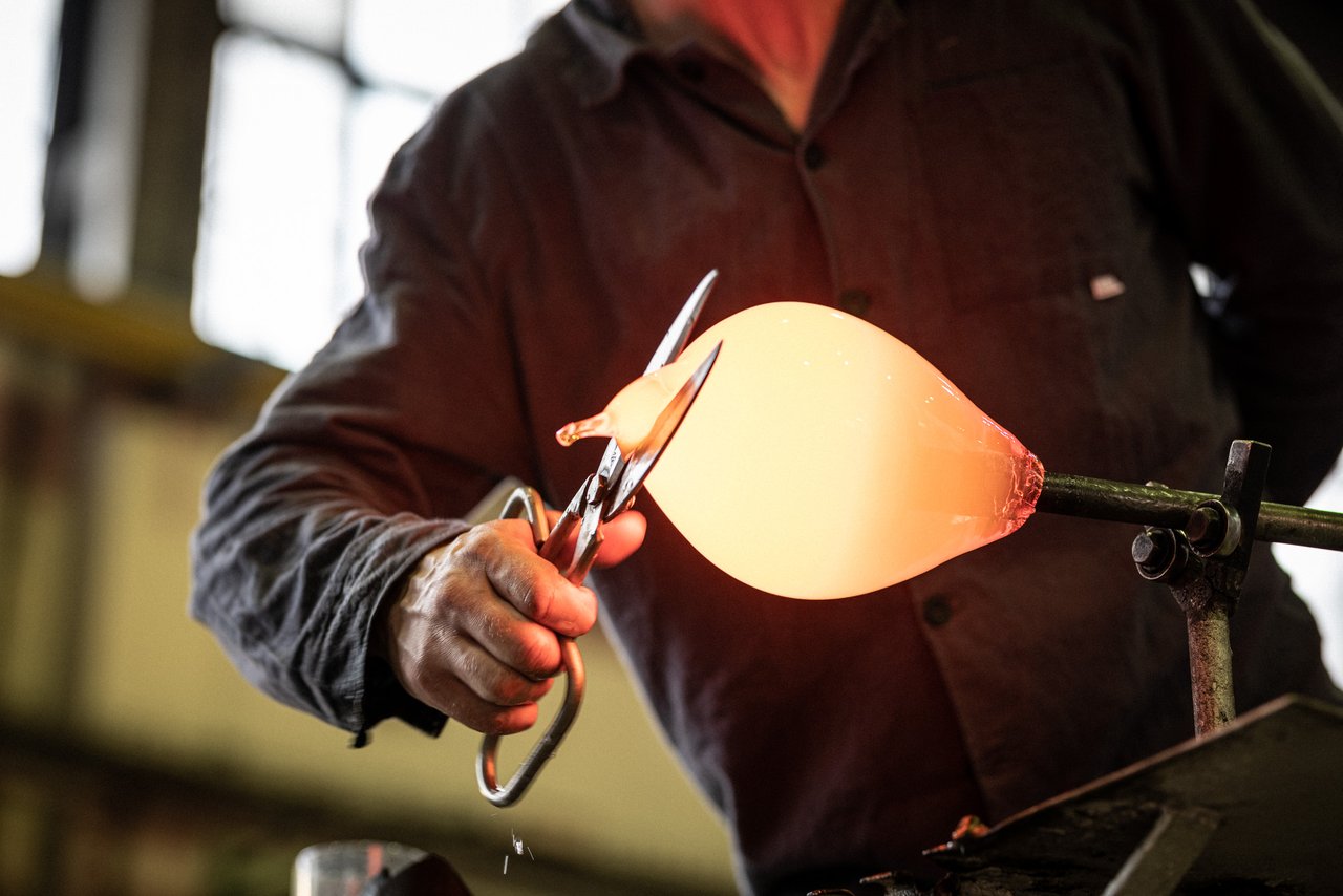 Un artisan utilisant un grand ciseau pour travailler du verre chaud de couleur orange