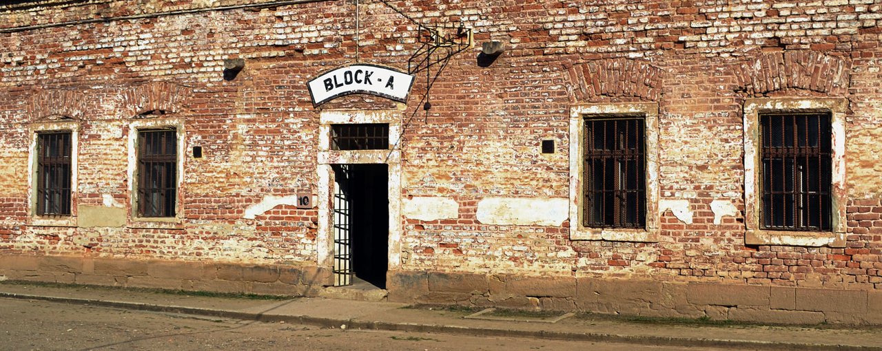 La façade d'un immeuble en briques rouges abimés,avec des fenêtres grillagées et une entrée portant l'inscription «BLOCK-A"