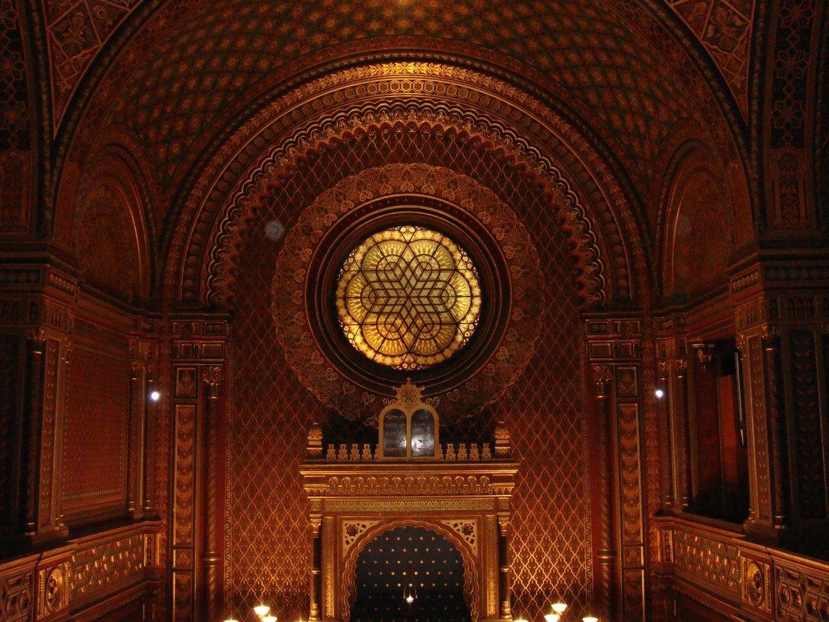 une salle monumentale, baignée d'une lumière dorée du crépuscule, dont les murs et les vitraux sont ornés de motifs sculpté