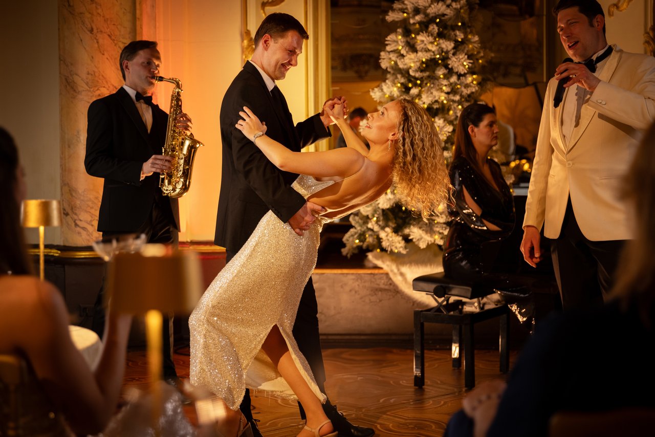 Une femme en robe blanche et un homme en costume noir qui danse avec des musiciens en fond