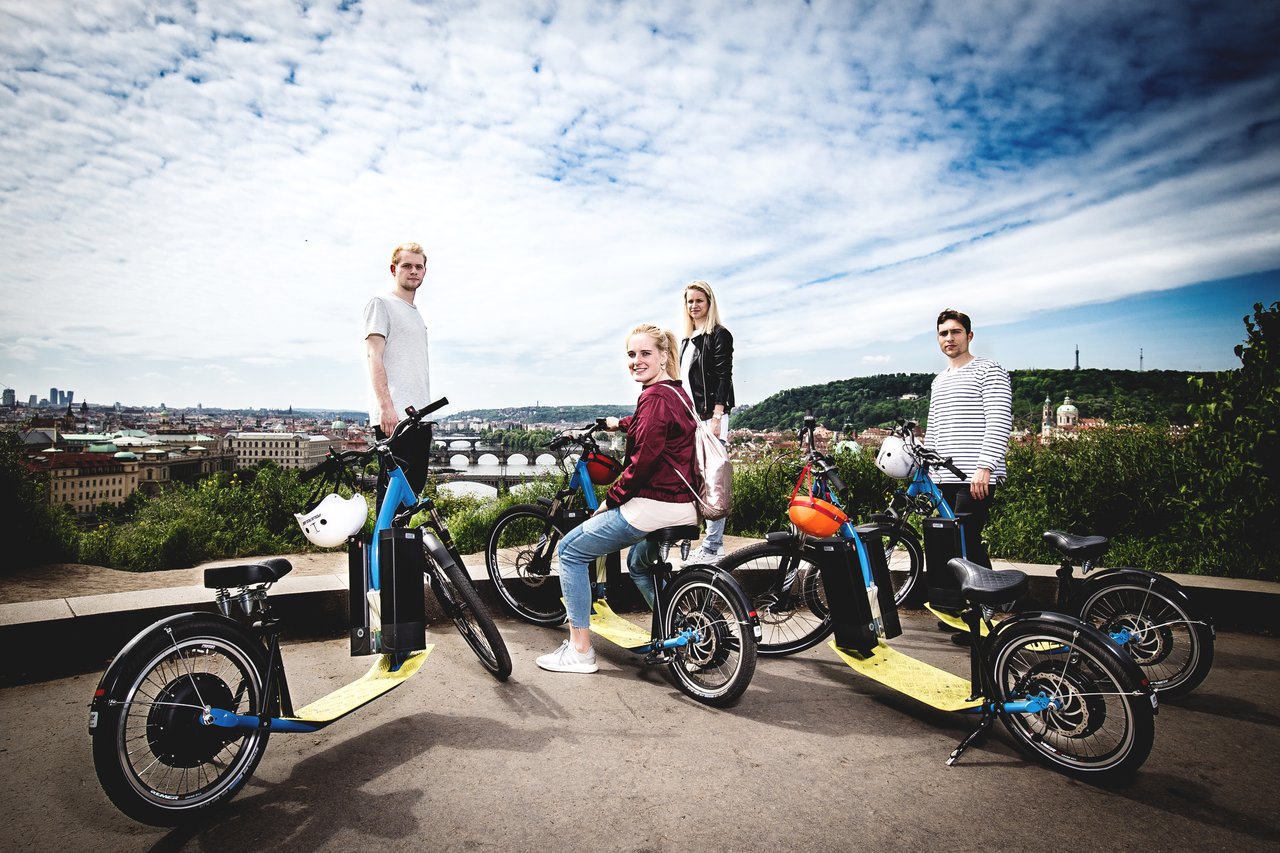 4 personnes sur et à côté d'un trottinette électrique, avec une vue sur la ville
