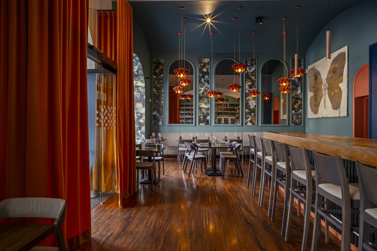 Intérieur du restaurant une longue table à droite et un tableau de papillon sur le mur et des rideau rouge sur la gauche