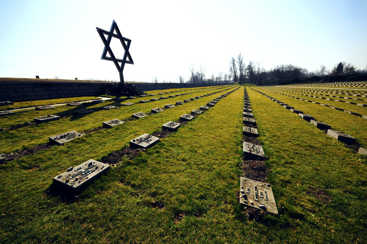 Des centaines de pierres tombales dans le cimetière, dominées par une grande étoile de David en métal sous un ciel dégagé.