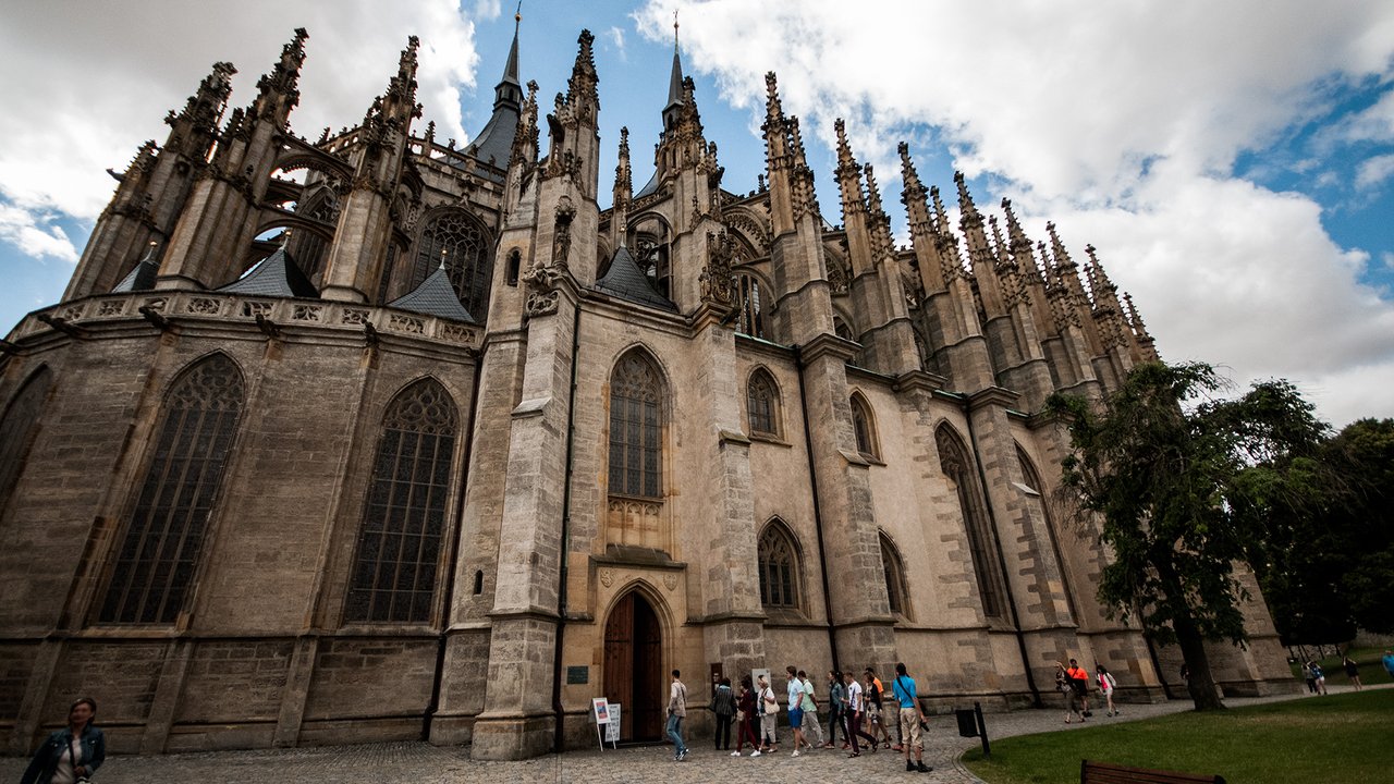 Une imposante façade en pierre beige  avec une multitude de flèches pointues et sculptées avec de grandes vitraux