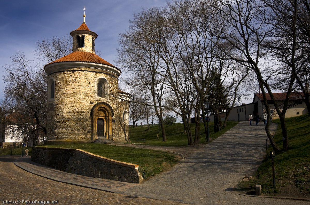 Une petite église ronde en pierres claires avec un toit de tuiles orange s'élève à côté d'un chemin pavé entouré d'