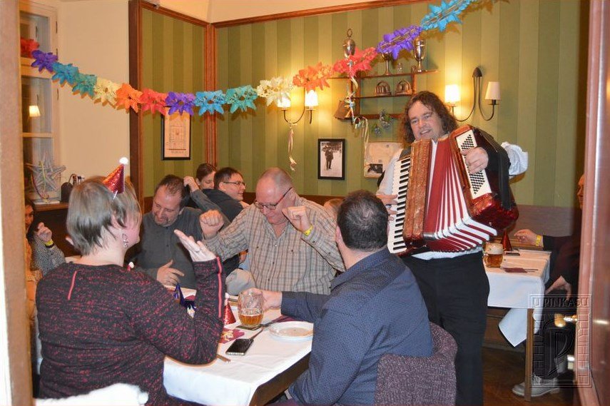 Un monsieur qui joue de l'accordéon dans une brasserie, il y a le public assis qui danse