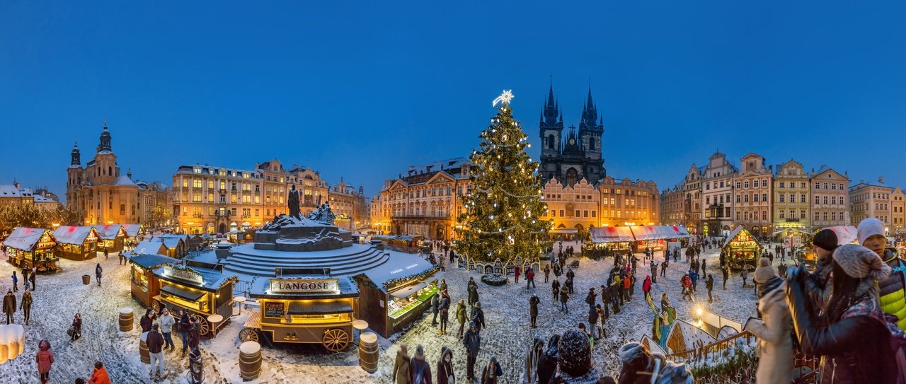 Un grand marché de Noël avec un immense sapin décoré en son centre, la nuit tombe et la ville s'illumine