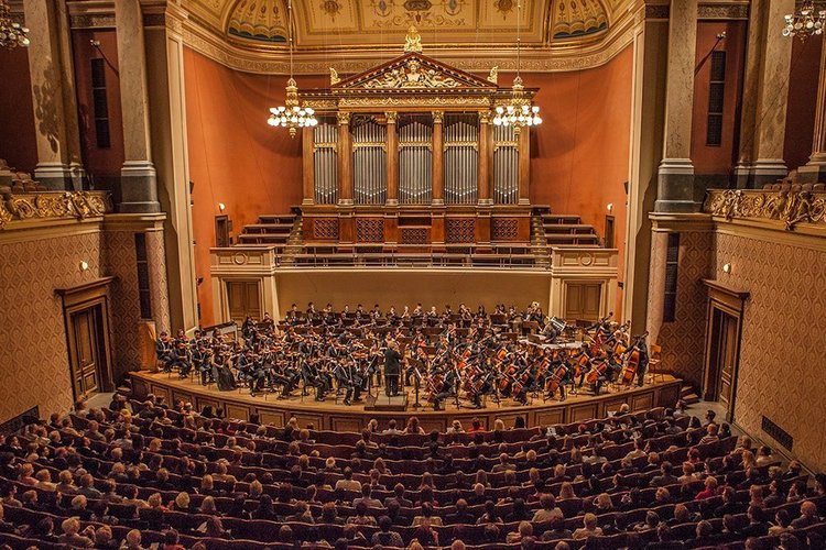 Grande salle avec un grand orgue il y a un concert avec beaucoup de musiciens et beaucoup de publics