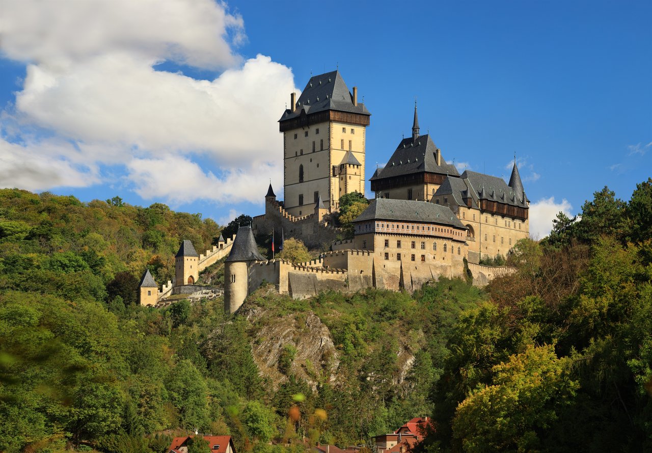 Une forteresse gothique beige, dotée de cinq petites tours et de toits noirs, située sur une colline