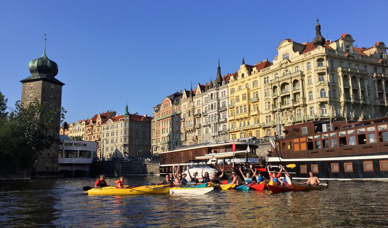 Groupe de gens en kayak qui sont content en fond on peut voir des gros bateaux et la ville derrière