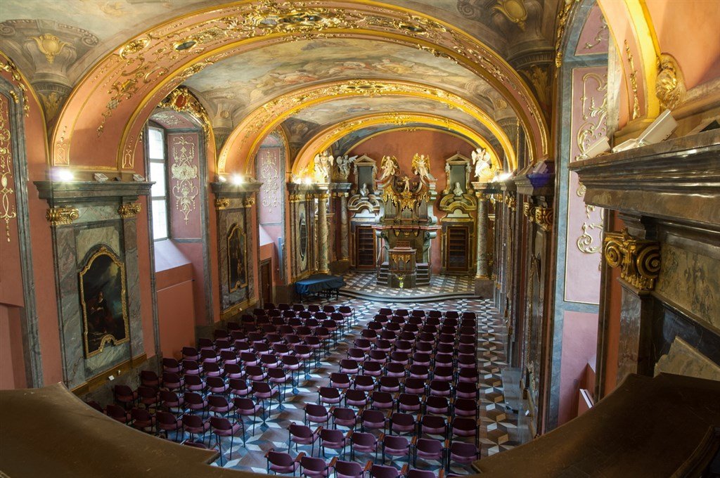 Grande rangée de chaise dans une chapelle aux murs colorées et ornées d'or